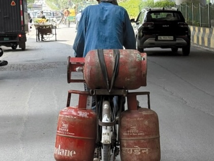 A man transports multiple LPG cylinders on a bicycle along a busy road in New Delhi, India.