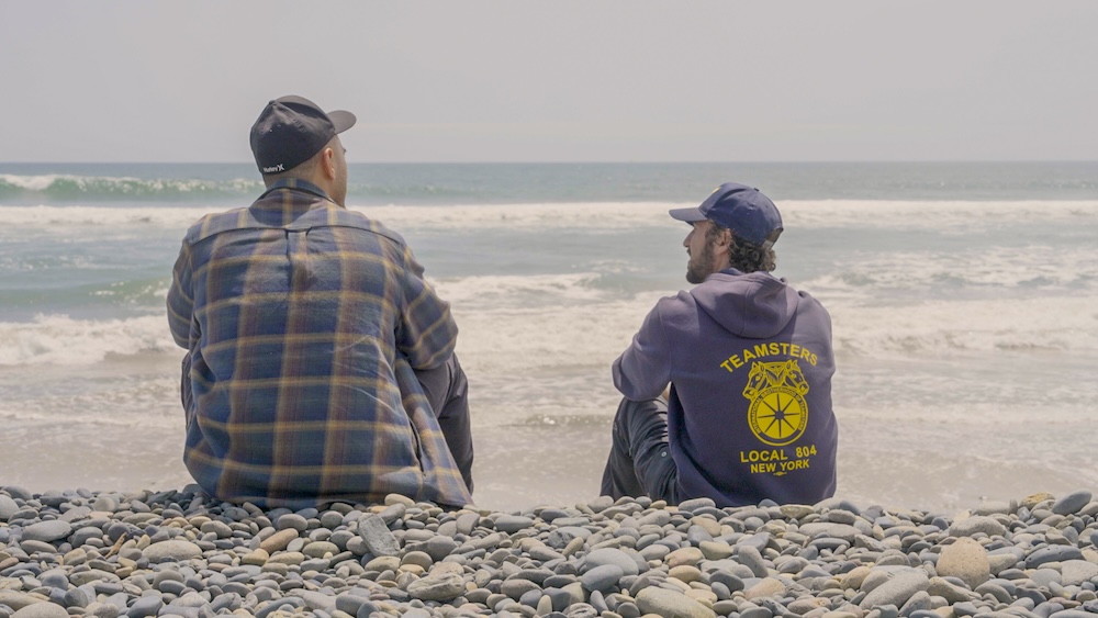A still featuring two UPS workers sitting together on a beach, from the 2026 documentary Who Moves America