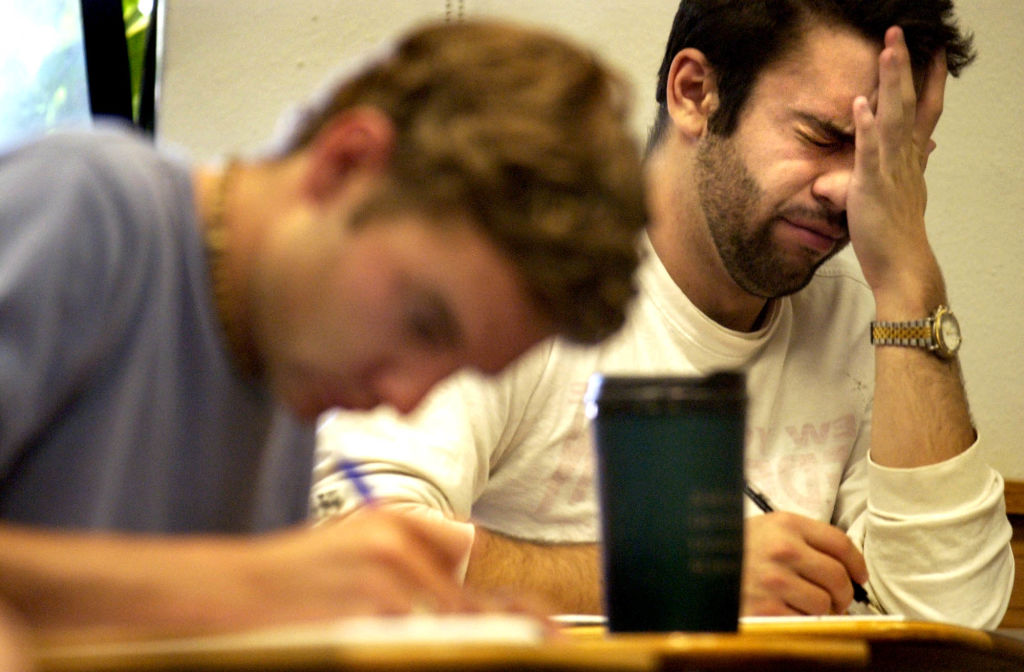 Two college students, one visibly exhausted, work at a desk. 