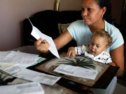 A woman looks over one of the many bills piled on her living room table.