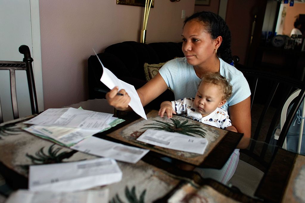 A woman looks over one of the many bills piled on her living room table.